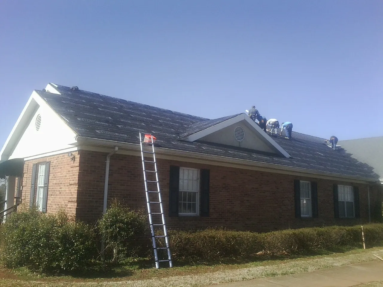 Crew tearing shingles off a brick ranch roof with a ladder set — Metal Roof Repair work by our crew in Greenwood Lake