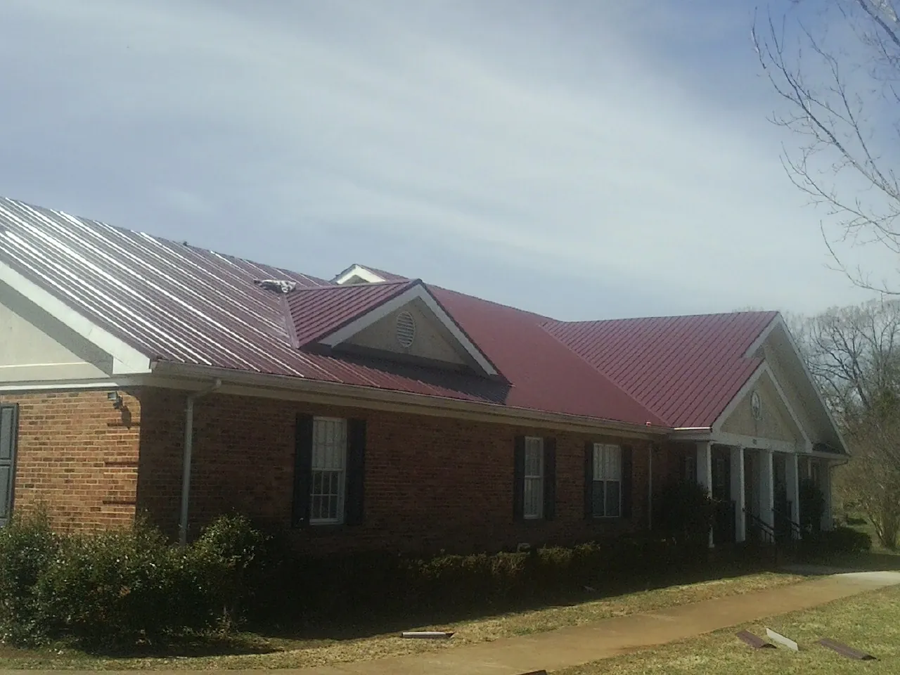 Red metal roof with gabled entries on a long brick building, from a Hail Damage Roof Repair job in Greenwood Lake