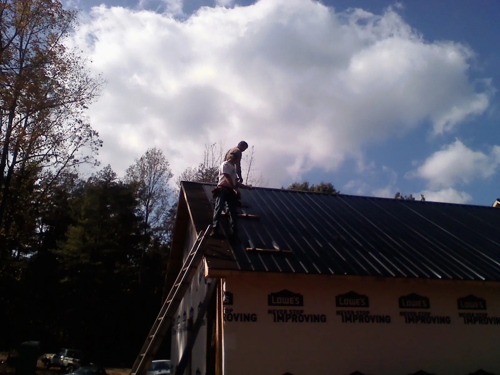Roofer fastening dark metal panels high against a cloudy sky, from a Roof Inspection job in Greenwood Lake