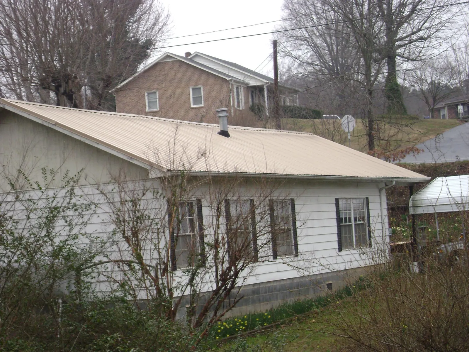 Tan metal roof on a white sided house set into a hillside — Commercial Roofing by Roofing Brothers in Greenwood Lake